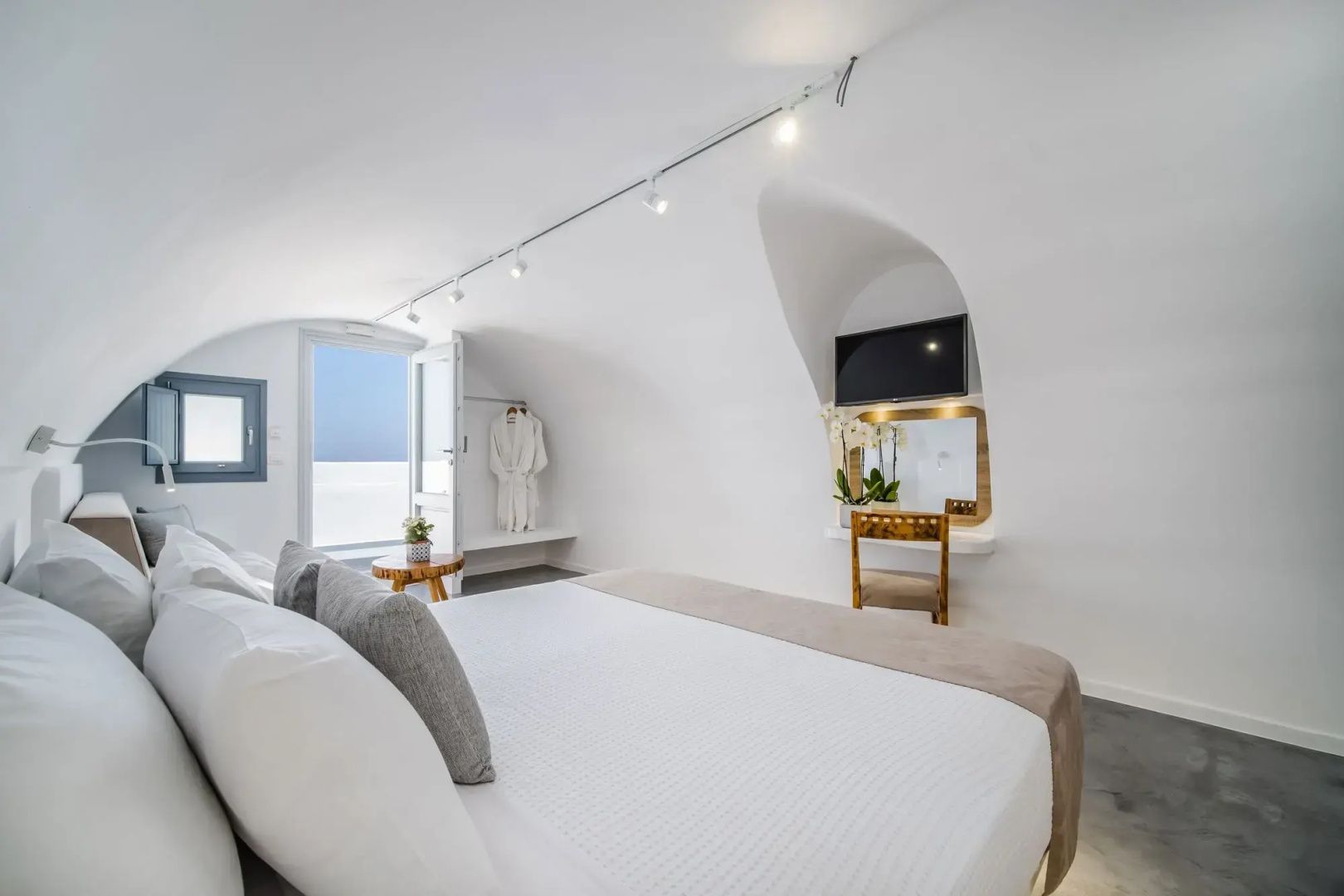 Helles Zimmer mit Doppelbett, Wand-TV, Frisiertisch und Zugang zum Außenbereich.
