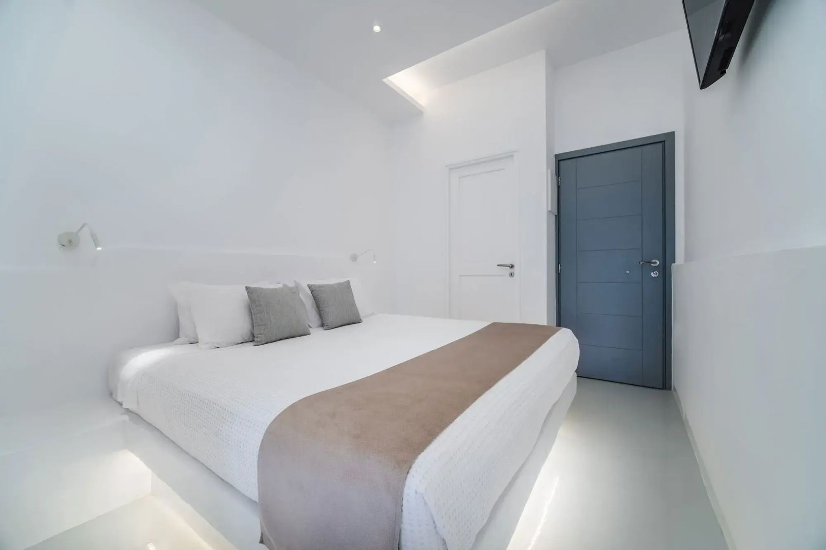 Weißes Schlafzimmer mit Doppelbett, indirekter Deckenbeleuchtung und blau grauer Eingangstür.