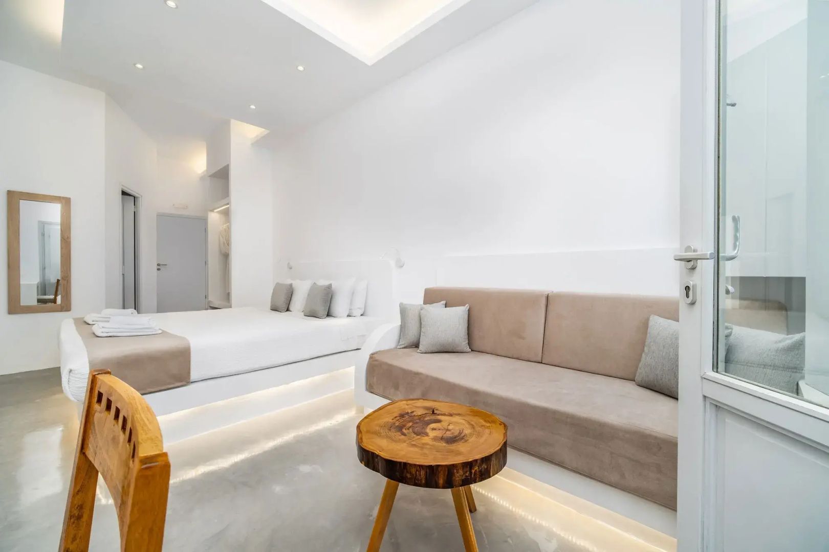 Moderne Suite mit weißem Bett, beigefarbenem Sofa und einem runden Holztisch.