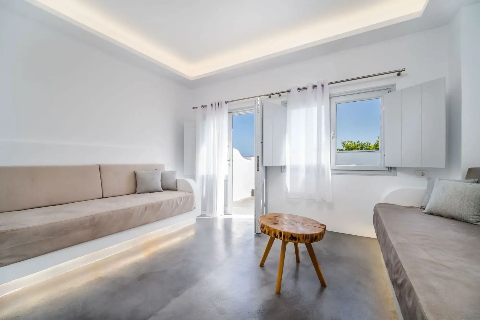Heller Wohnbereich mit beigem Sofa, einem kleinen Holztisch und Zugang nach draußen.