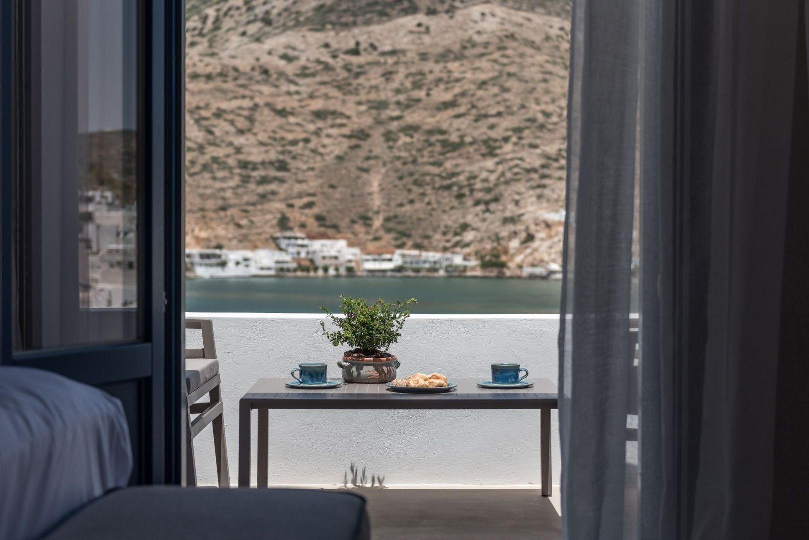 Blick von der Terrasse mit Tisch und Kaffeetassen auf die Bucht und Hügellandschaft.
