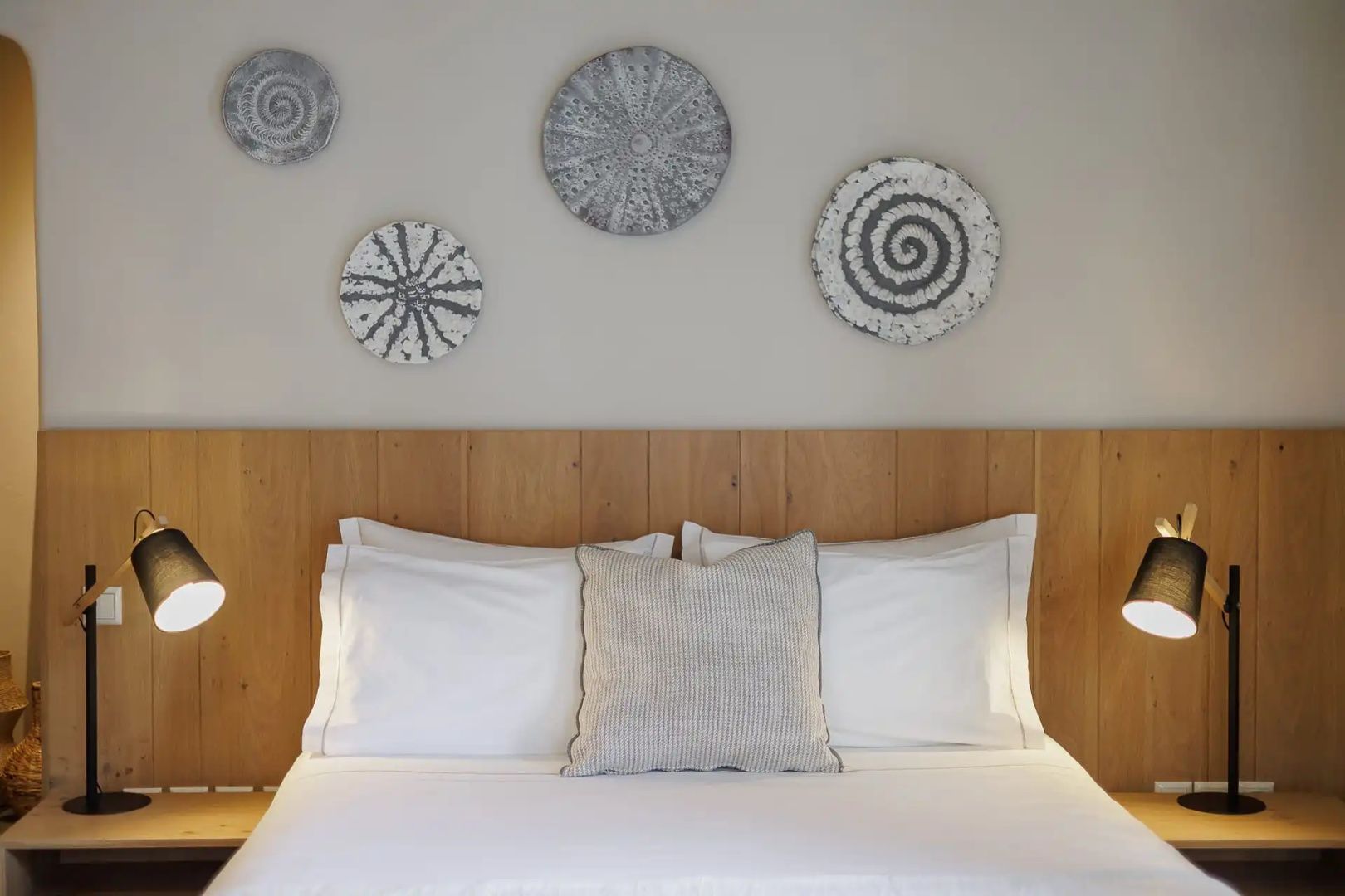 Doppelbett mit Holz-Kopfteil, weißen Kissen und runder Wanddekoration in einem Hotelzimmer.