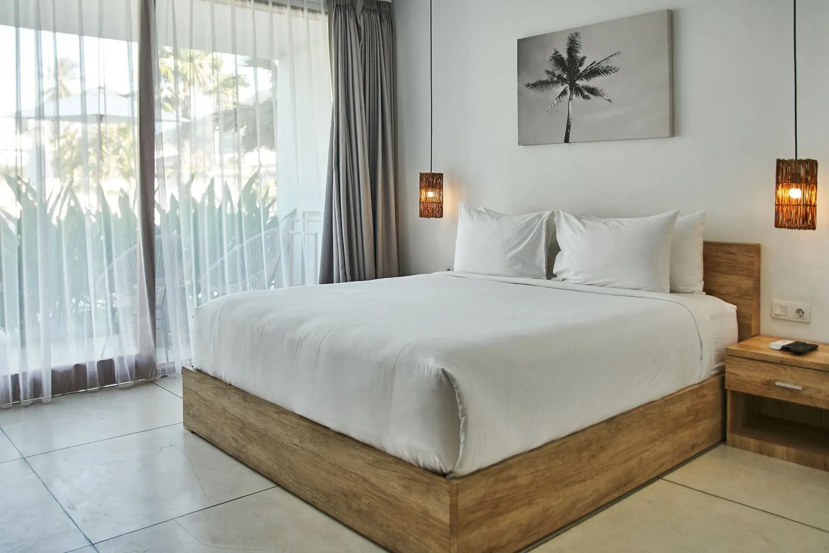 Doppelbett mit Holzrahmen, weißer Bettwäsche und Vorhängen im hellen Hotelzimmer.