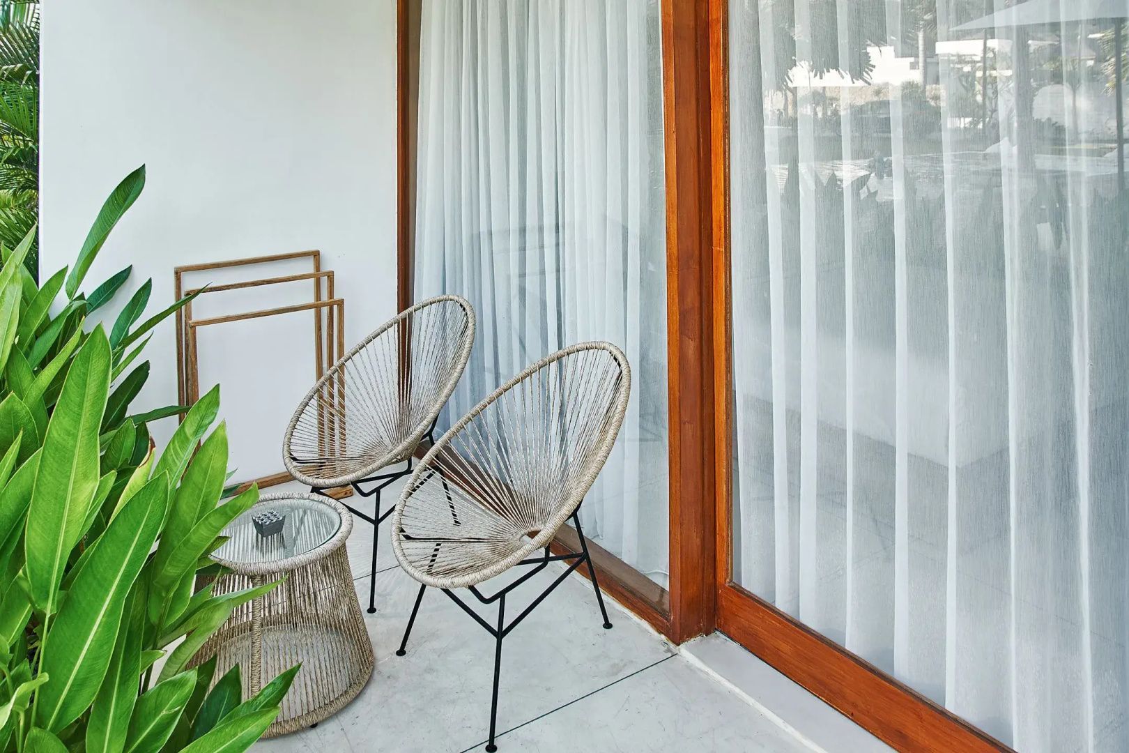 Terrasse mit zwei Stühlen aus Geflecht, einem kleinen Tisch und großem Fenster.