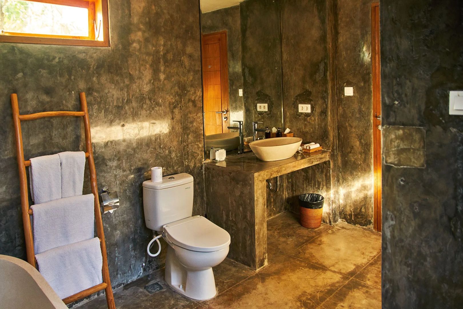 Badezimmer in grauer Betonoptik mit Toilette, Waschtisch und Handtuchhalter aus Holz.