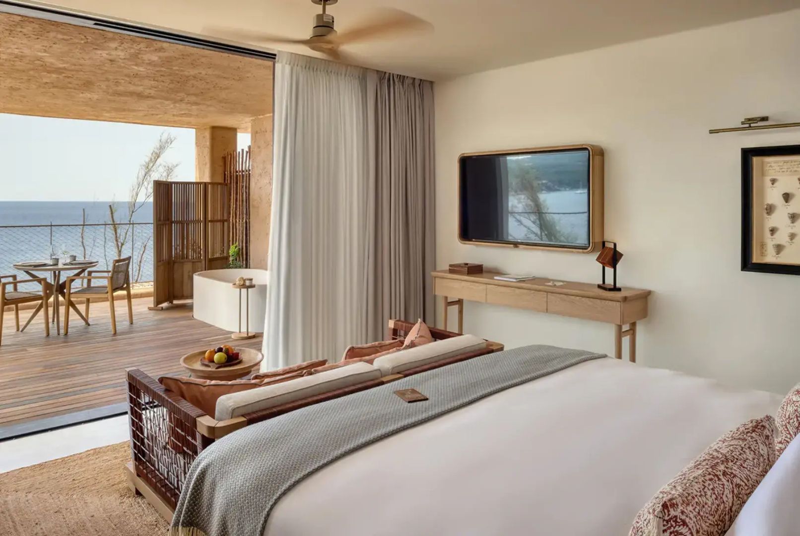 Helles Hotelzimmer mit Doppelbett, Fernseher an der Wand und Zugang zur Terrasse mit Badewanne.