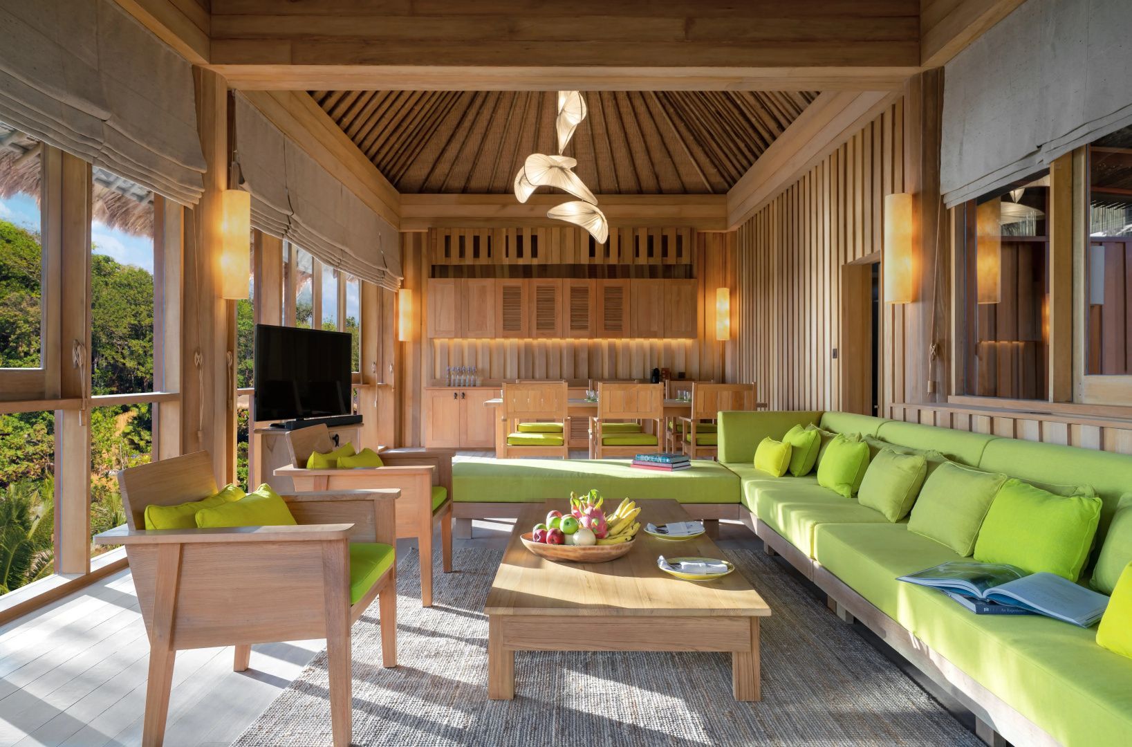 Wohnbereich einer Villa aus Holz mit grüner Couch, Holztisch und Essplatz im Hintergrund.