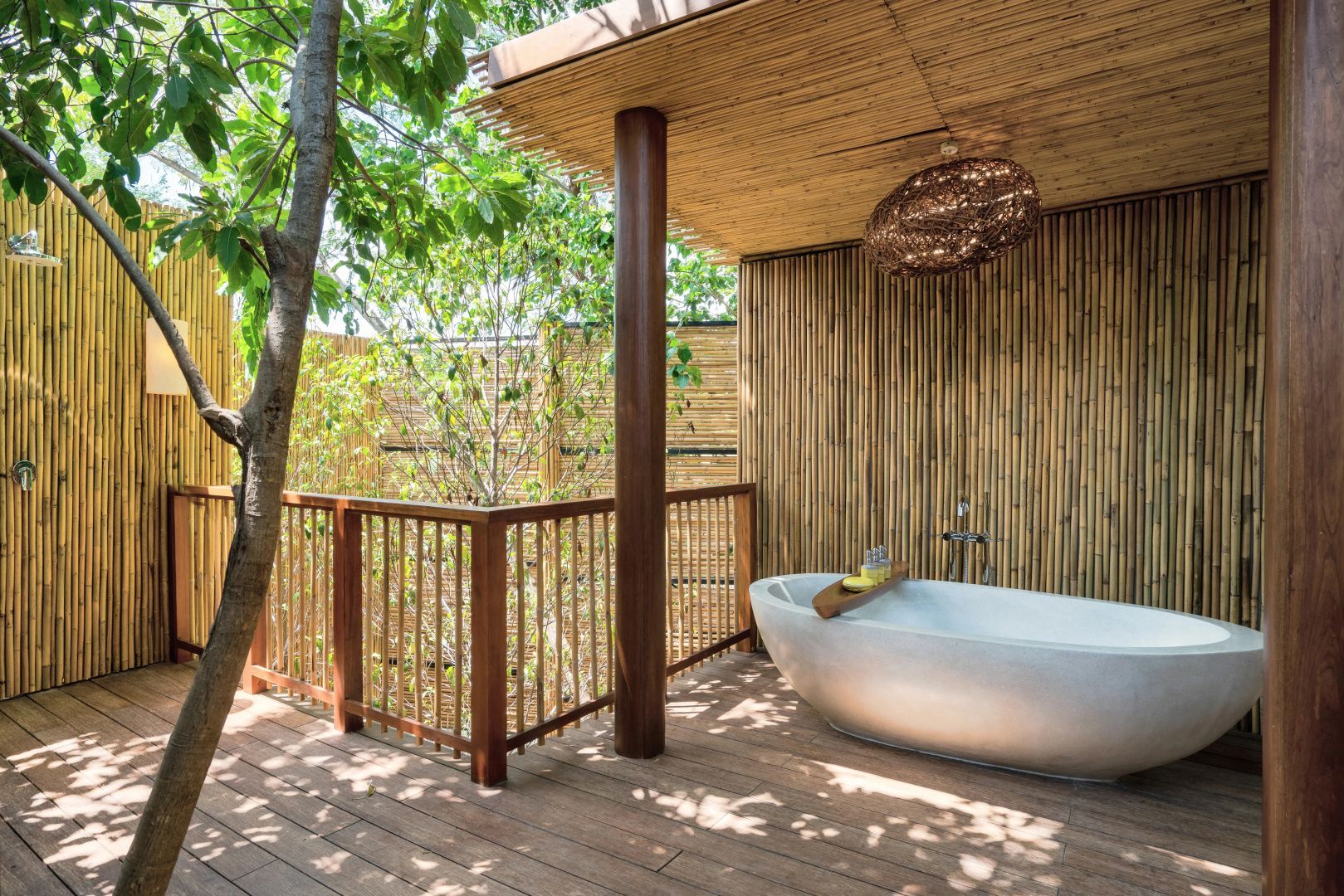 Freistehende Badewanne auf einer überdachten Holzterrasse mit Bambuswand.