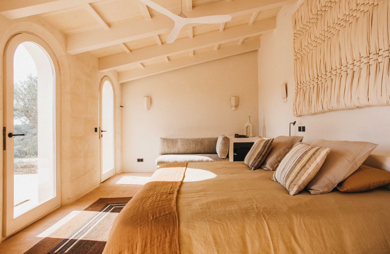 Helles Hotelzimmer mit großem Bett, Holzdeckenbalken und cremefarbenen Textilien.
