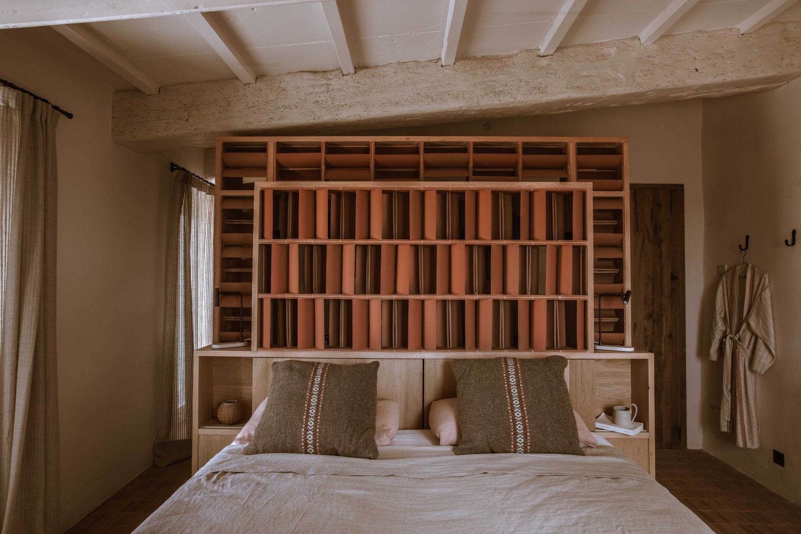 Doppelbett mit strukturiertem Kopfteil aus Holz und Ton sowie einer Holzbalkendecke.
