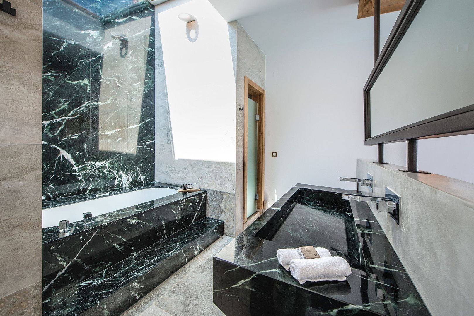 Badezimmer mit eingelassener Badewanne aus schwarzem Marmor und großem Doppelwaschtisch.