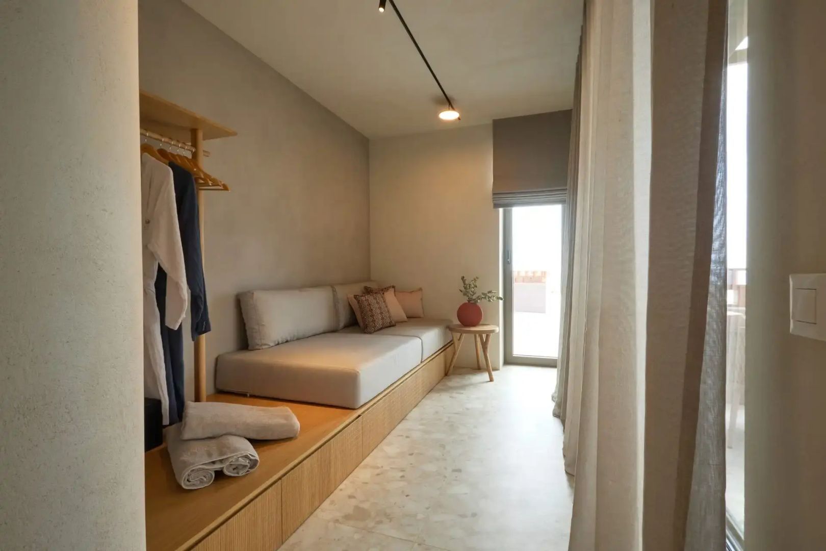 Sitzbereich im Hotelzimmer mit integriertem Sofa, Holzablage und hellem Vorhang.