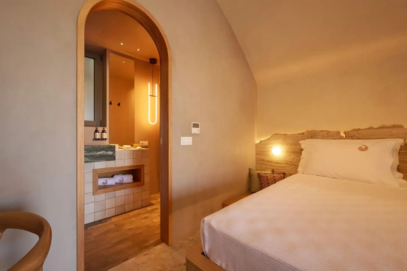 Blick vom Bett durch einen Rundbogeneingang in das angrenzende Badezimmer mit Waschtisch.