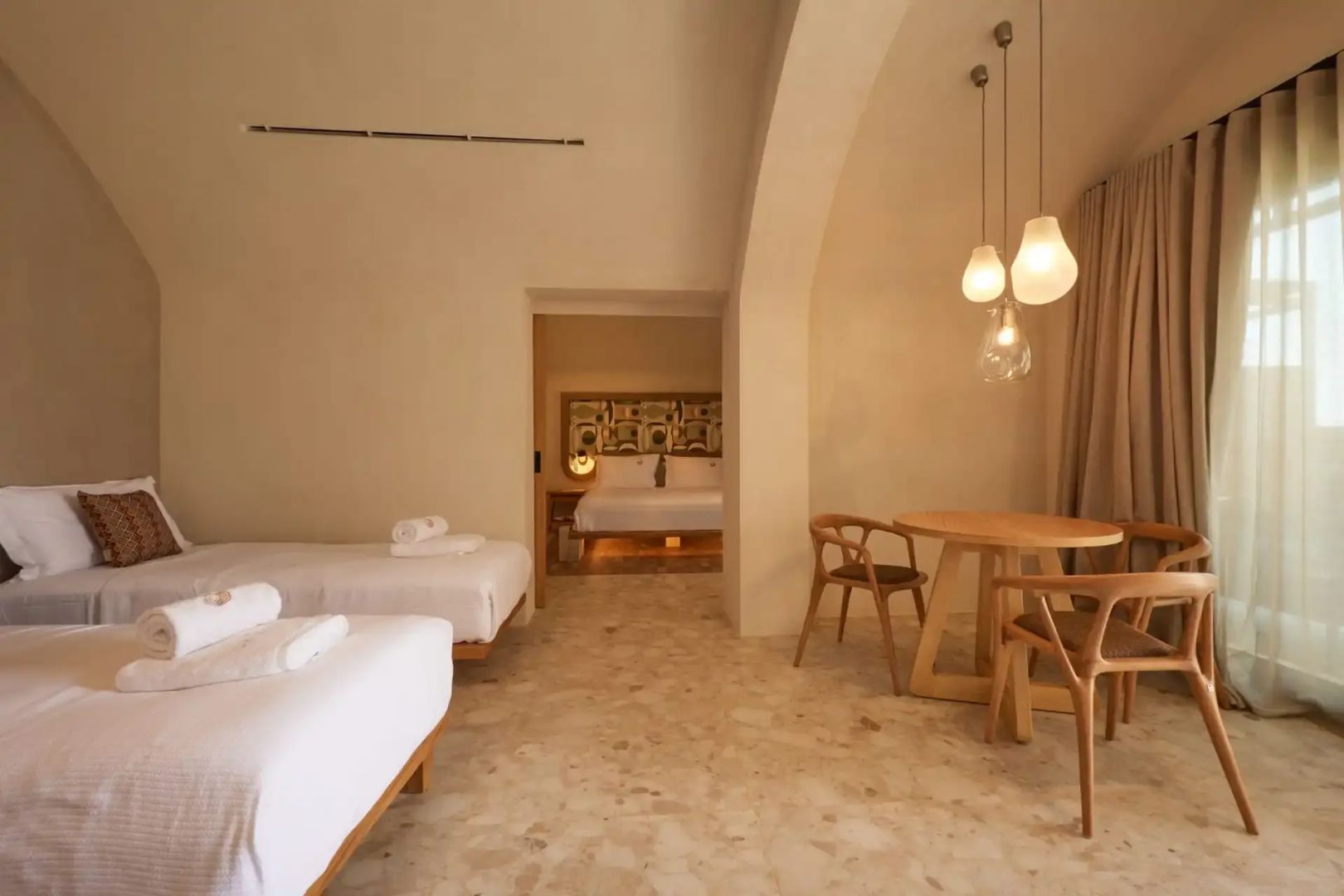 Hotelzimmer mit hölzerner Sitzgruppe, Betten und Durchgang zum nächsten Schlafraum.