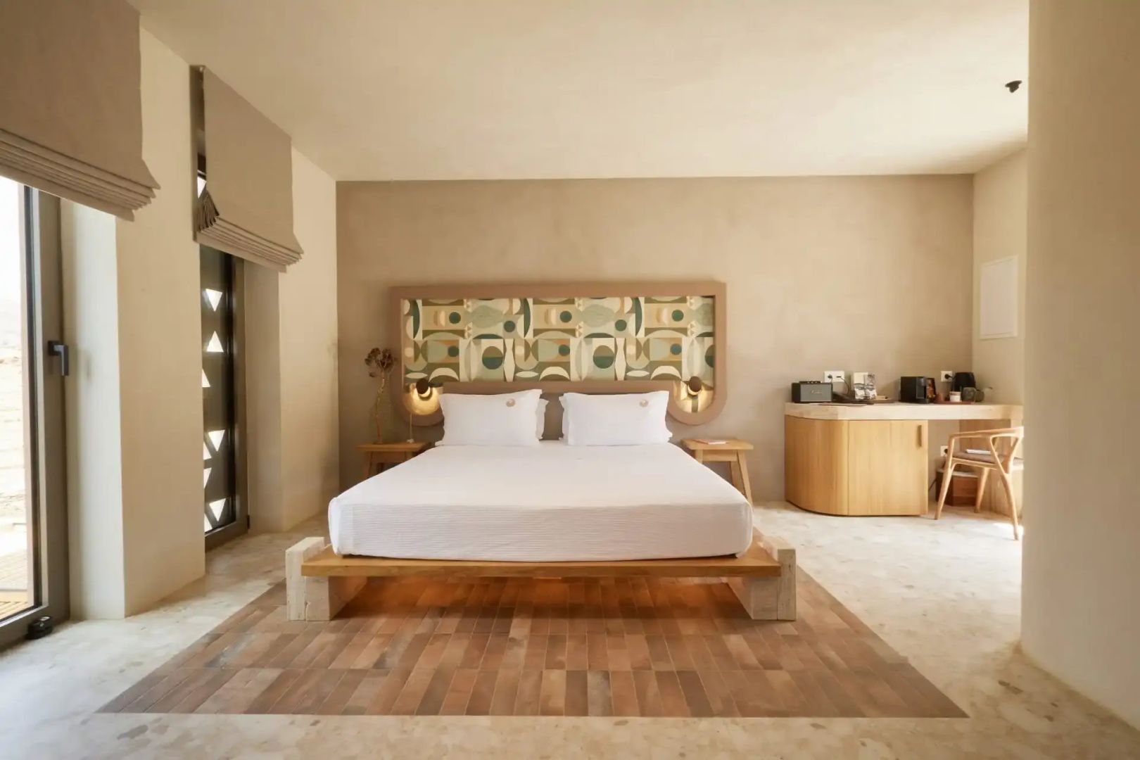 Helles Hotelzimmer mit Doppelbett, gemustertem Kopfteil und Holzfußboden unter dem Bett