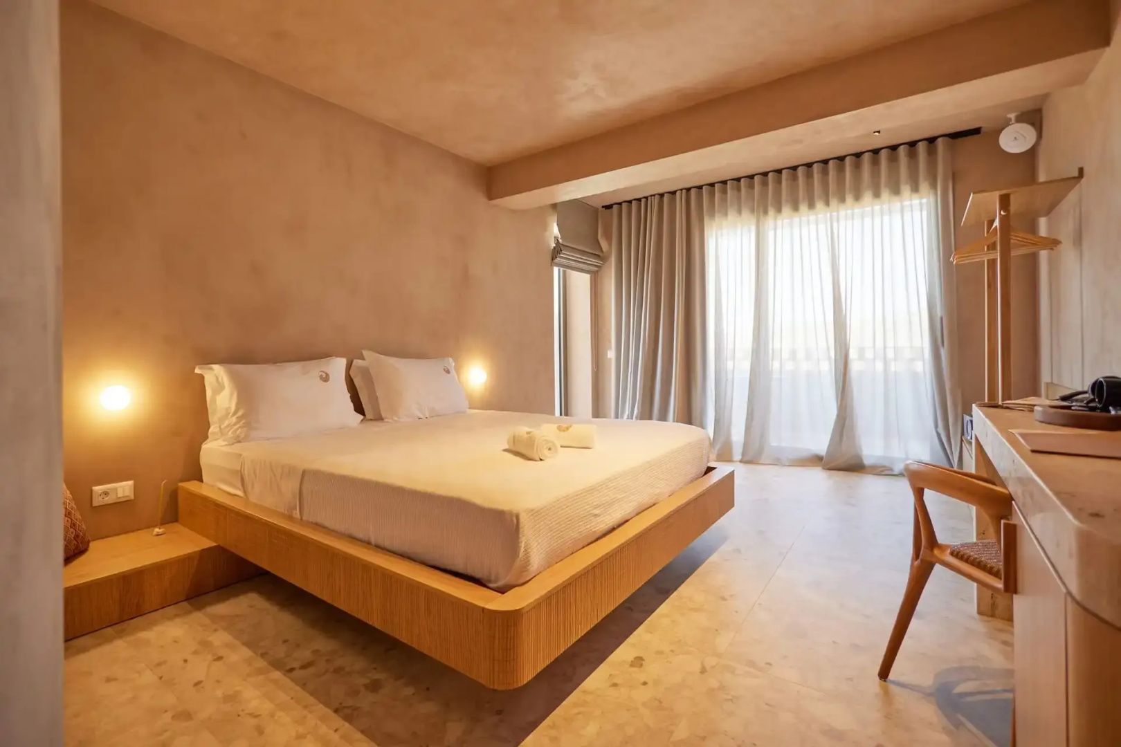 Doppelbett aus Holz in einem hell gestalteten Hotelzimmer mit Vorhängen