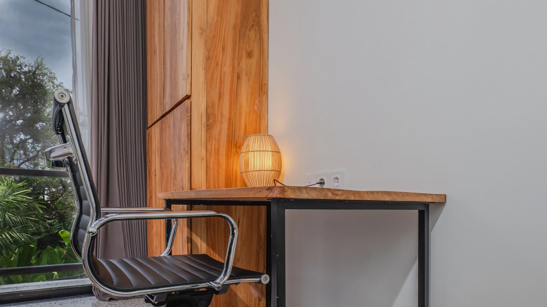 Arbeitsbereich aus Holz mit einem Bürostuhl, einer kleinen Lampe und Steckdosen an der Wand.