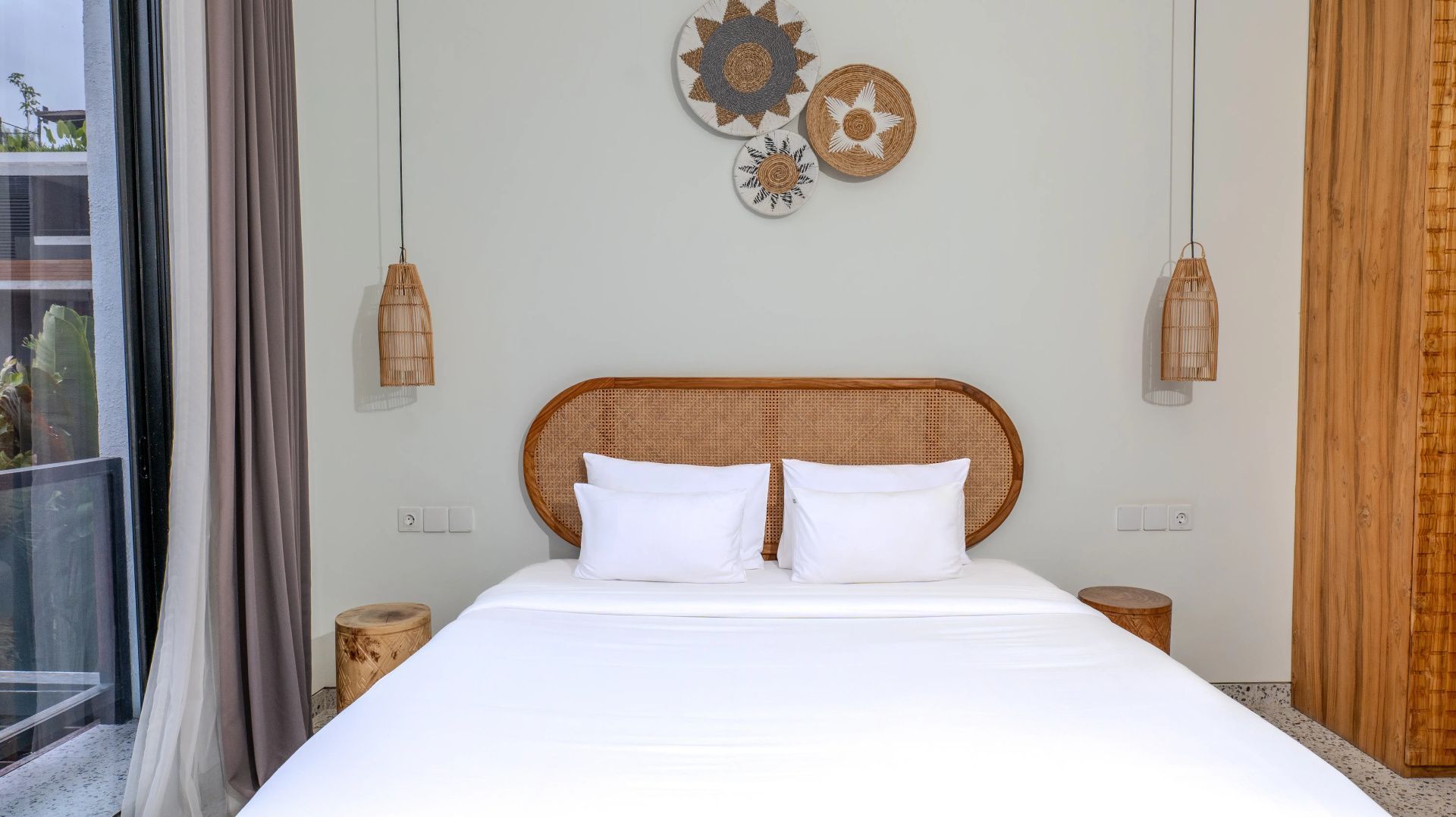 Doppelbett mit weißer Bettwäsche, Kopfteil aus Rattan und dekorativem Wandschmuck.
