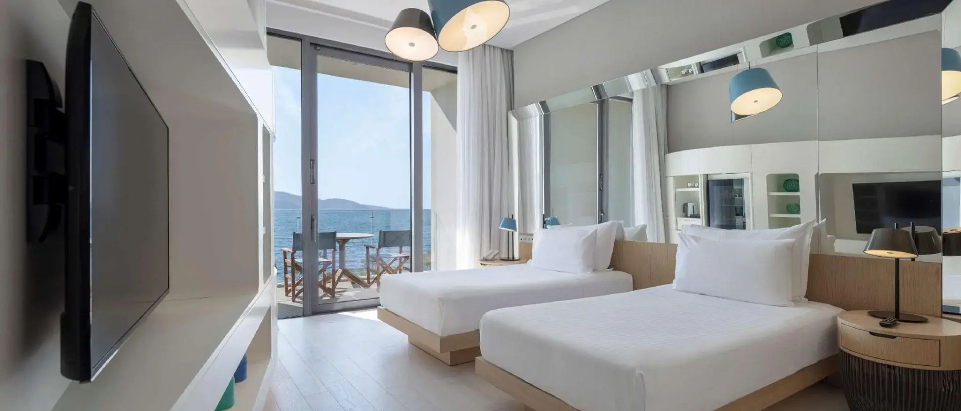 Hotelzimmer mit zwei Einzelbetten, großen Wandspiegeln und Zugang zum Balkon mit Meerblick.