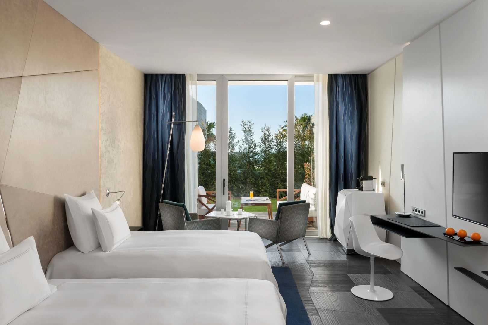 Schlafzimmer mit zwei Einzelbetten, Sesseln und Ausgang zum Gartenbereich.