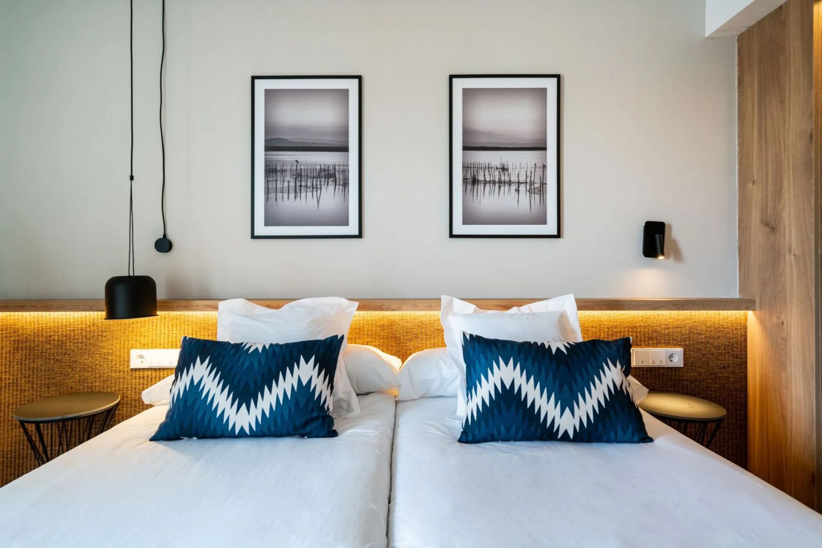 Doppelbett mit weißer Bettwäsche, blau gemusterten Kissen und zwei Wandbildern.