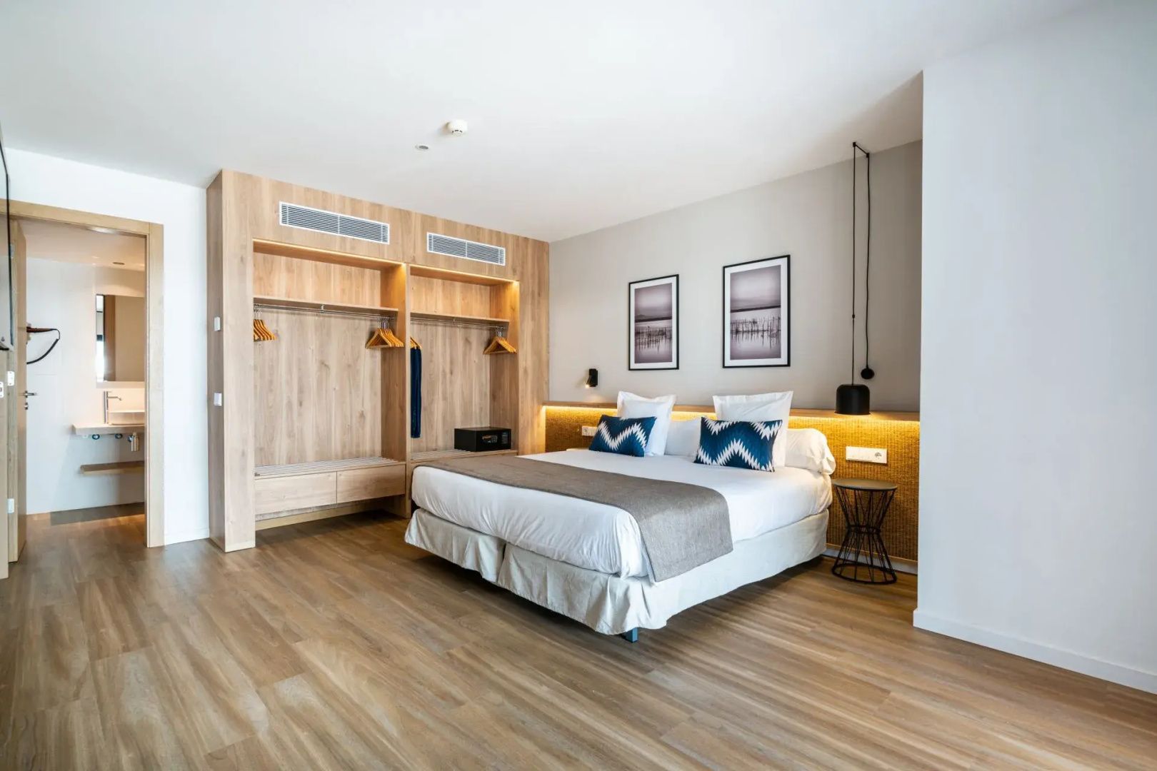 Modernes Schlafzimmer mit Doppelbett, Beleuchtung am Kopfteil und offenem Kleiderschrank aus Holz.