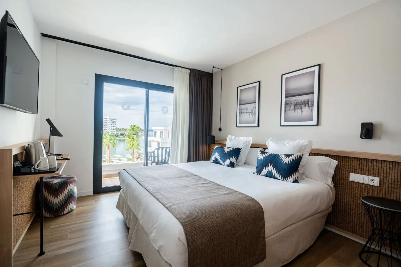 Helles Hotelzimmer mit großem Doppelbett und Blick durch die Balkontür.