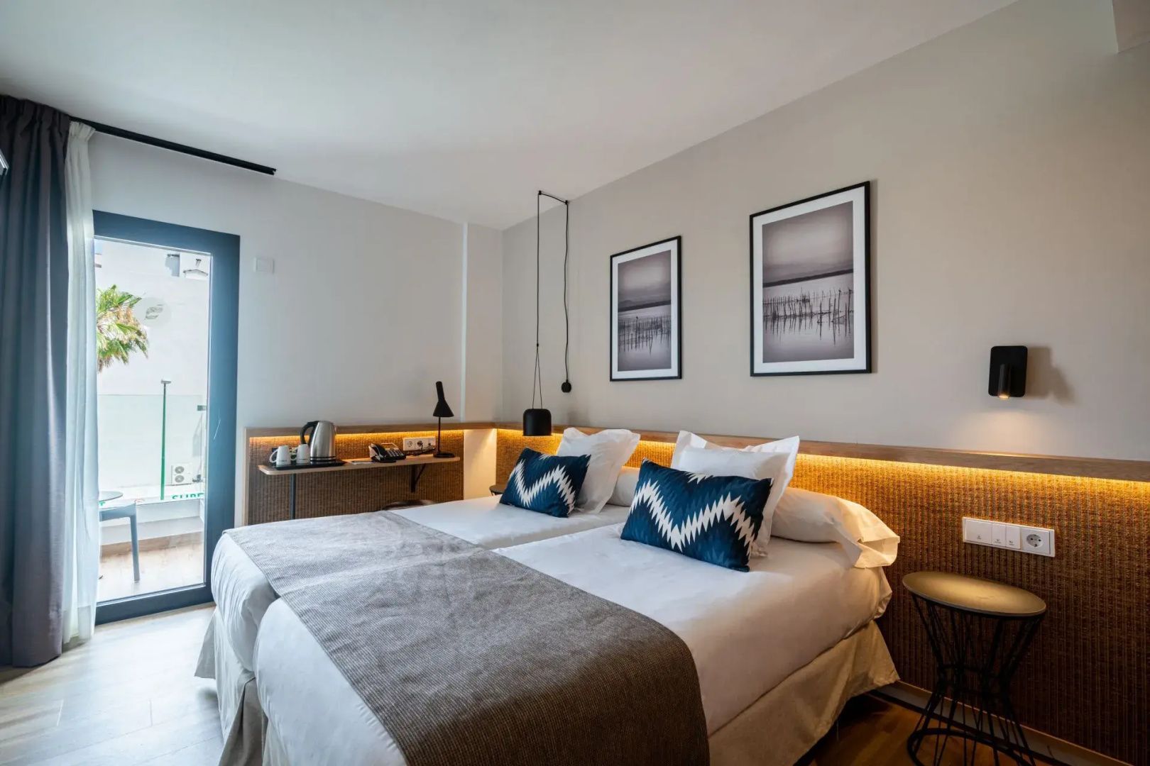 Hotelzimmer mit zwei zusammenstehenden Einzelbetten, Schreibtisch und Zugang zum Balkon.