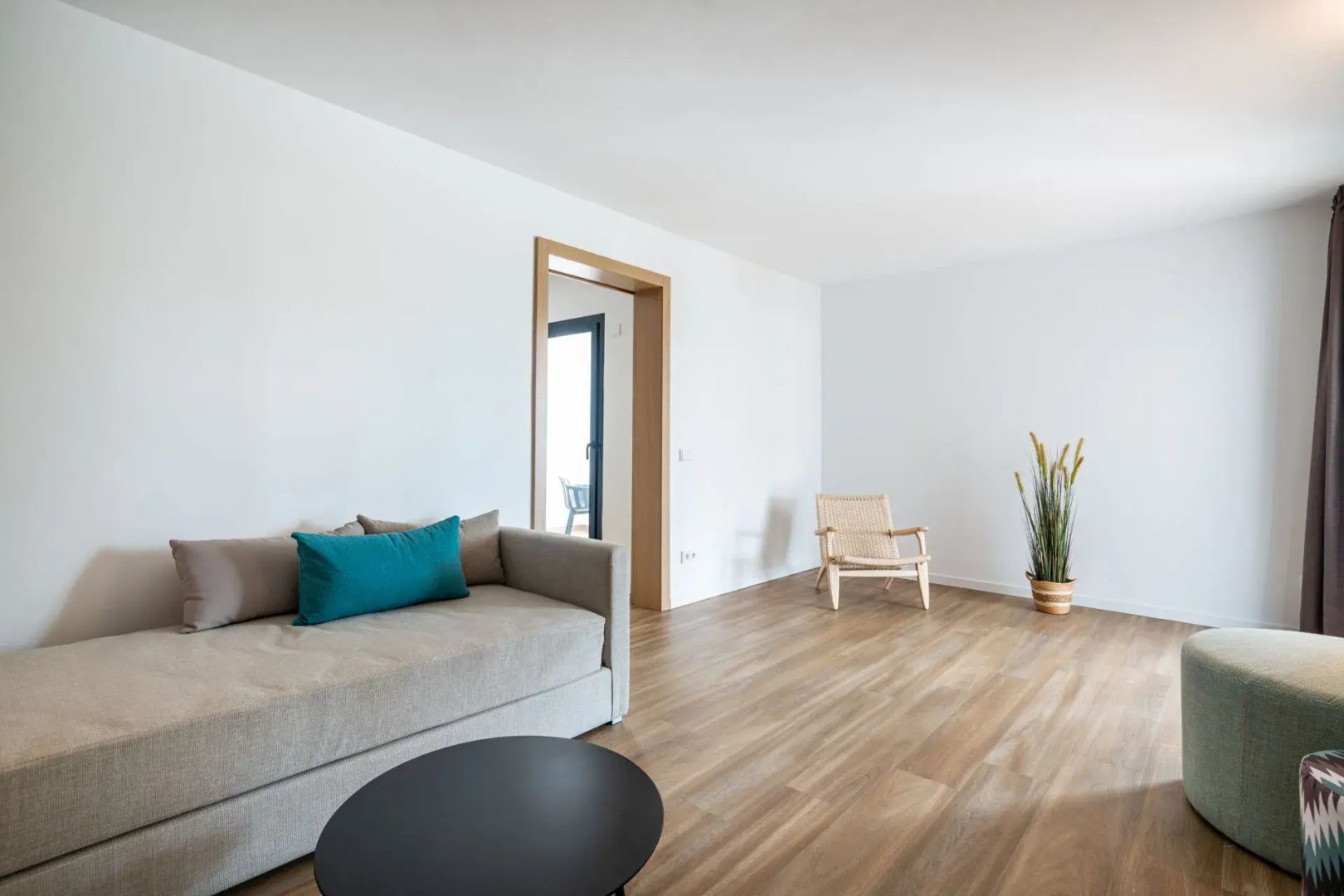 Heller Wohnbereich mit grauem Sofa, blauem Kissen, rundem Couchtisch und Holzstuhl.