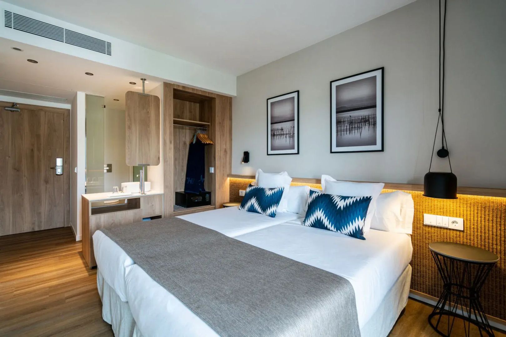 Doppelbett mit blau gemusterten Kissen, Holzschrank und Blick ins offene Badezimmer.
