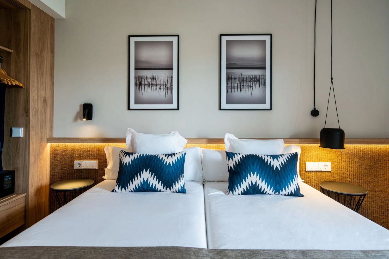 Doppelbett mit zwei blau gemusterten Kissen und zwei Wandbildern im Rahmen darüber.