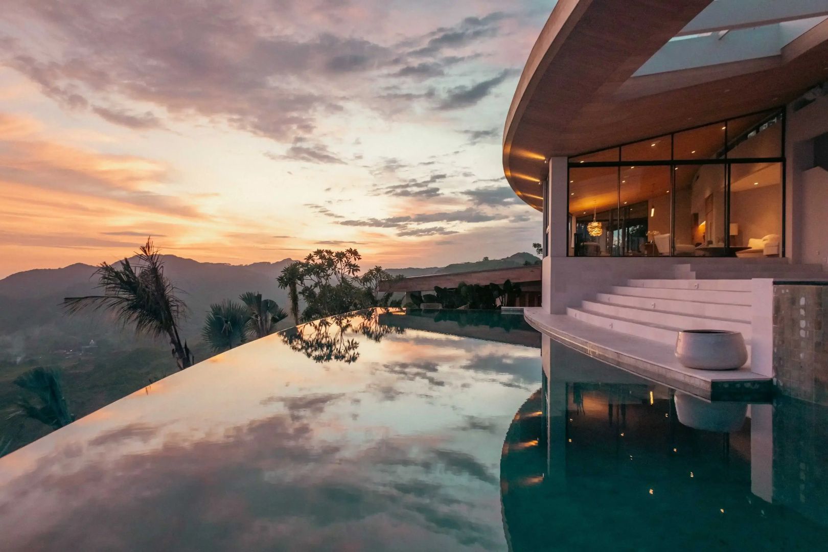Infinitypool einer Villa bei Abenddaemmerung mit Blick auf die umliegenden Huegel.