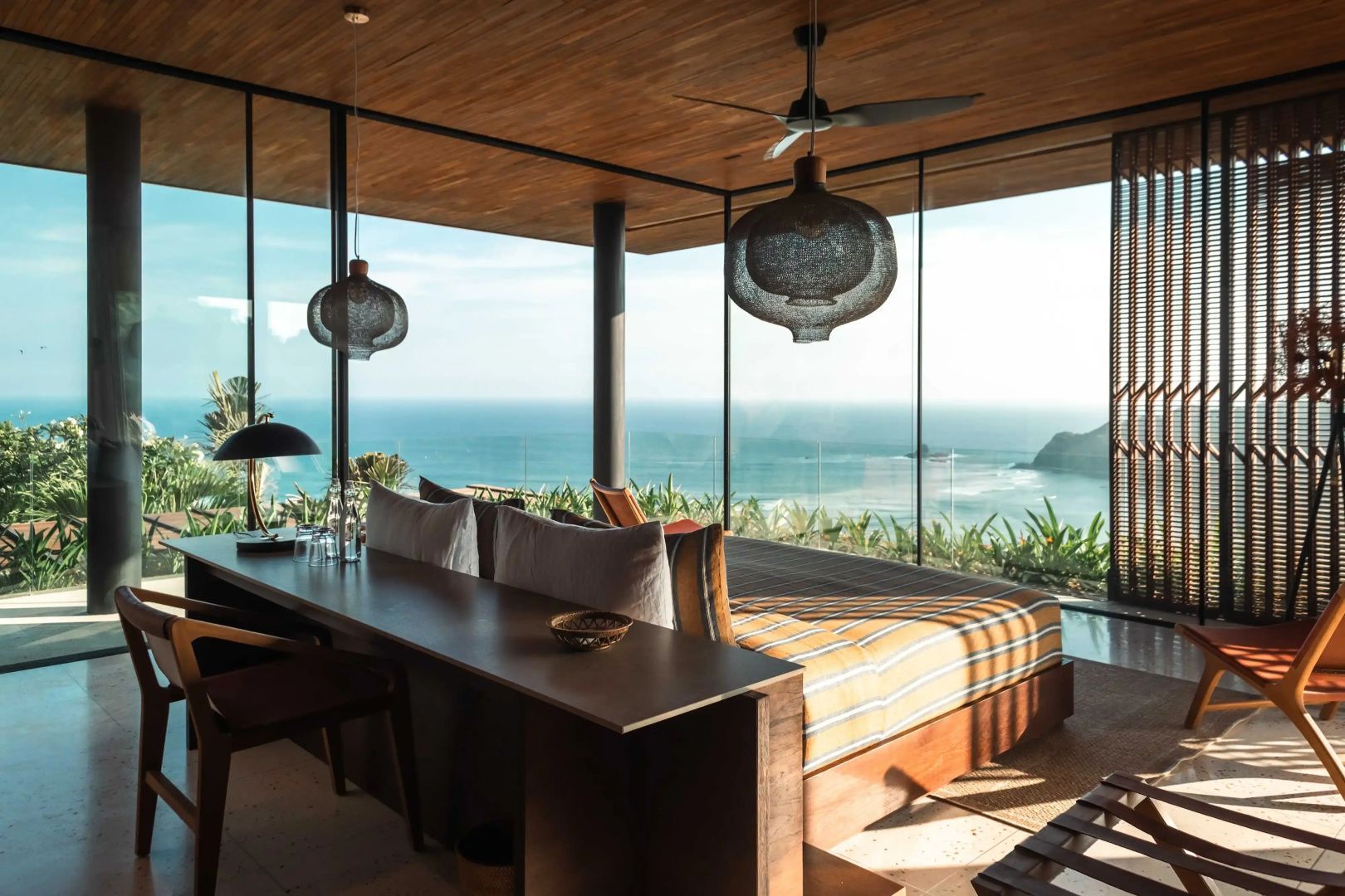Schlafbereich mit großer Glasfront und Blick auf das Meer und die Küstenlandschaft.