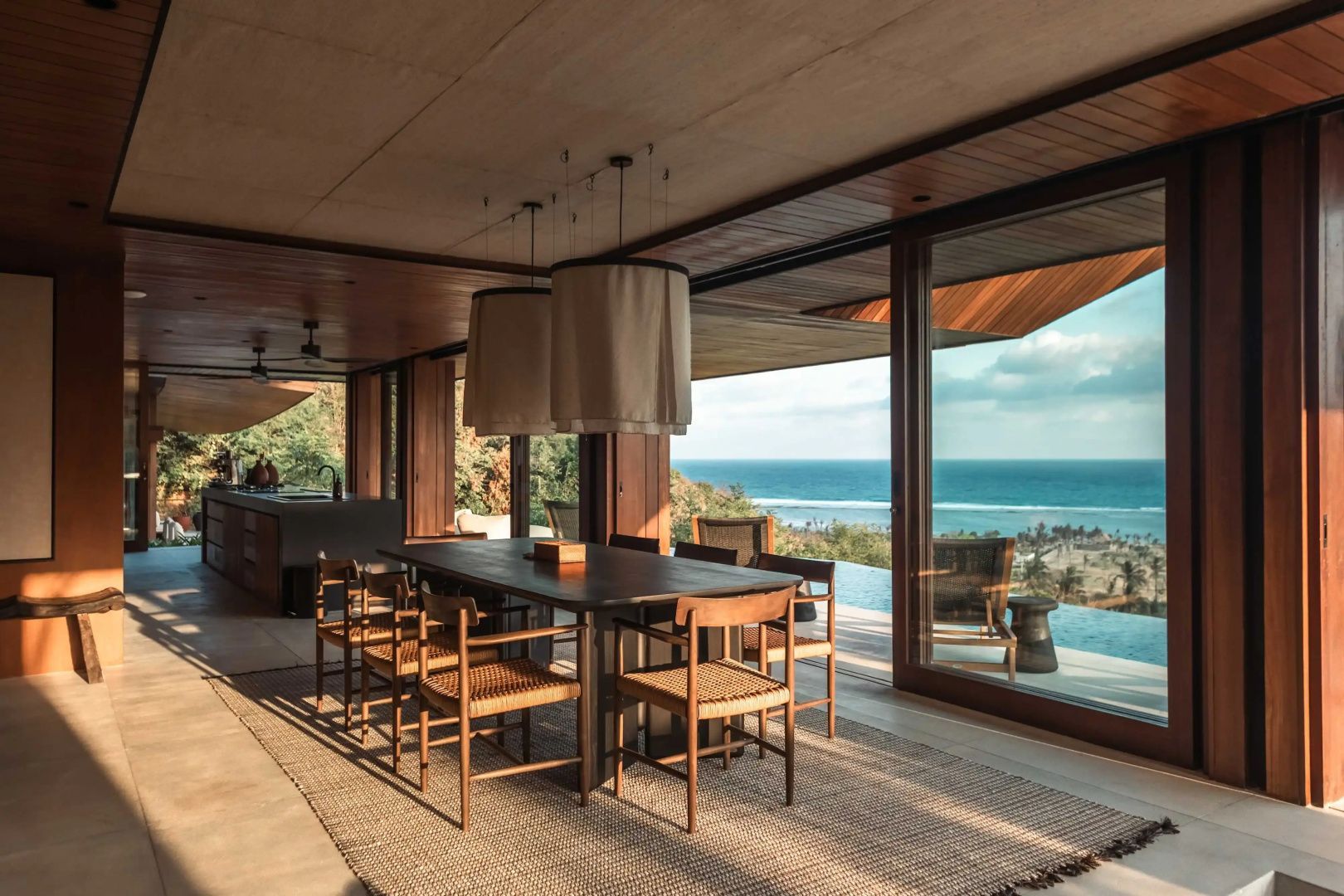 Offener Essbereich mit großem Holztisch und Stühlen sowie Blick auf das Meer.