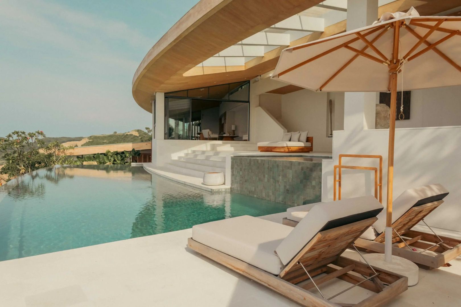Pool einer modernen Villa mit Sonnenschirm, Liegen und weißer Architektur im Tageslicht.