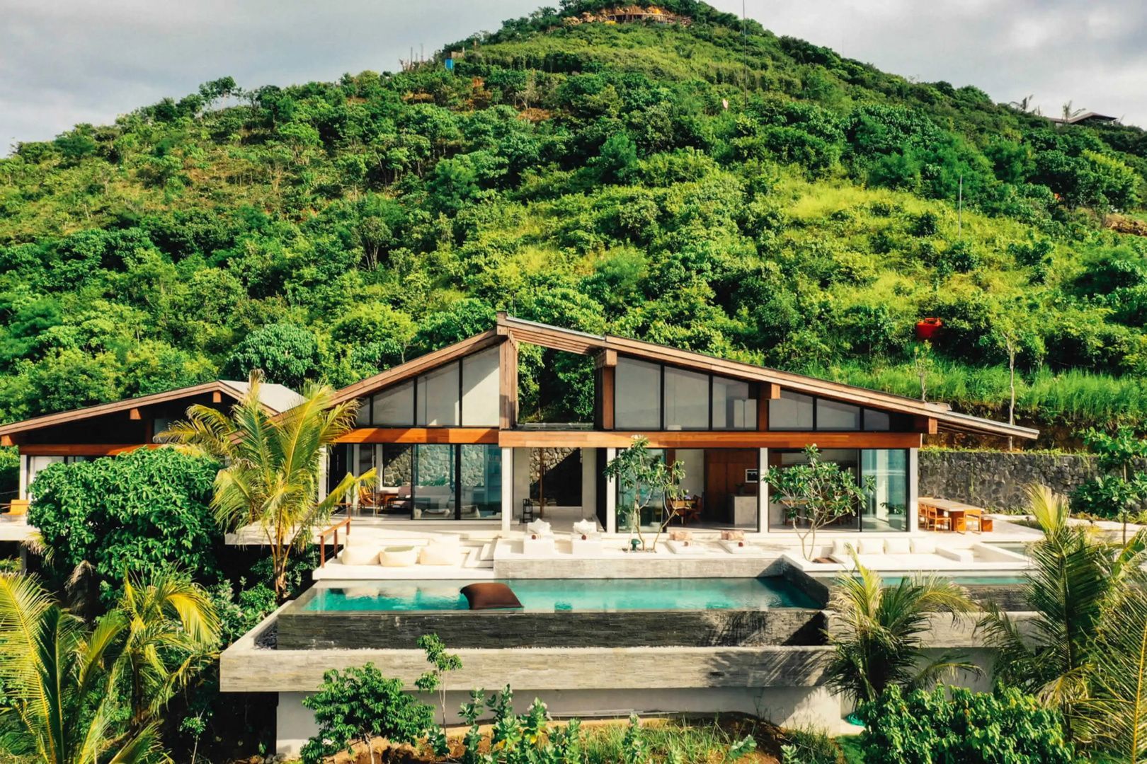 Moderne Villa mit Holz und Glasfassade, privatem Pool und grünem Hügel im Hintergrund.