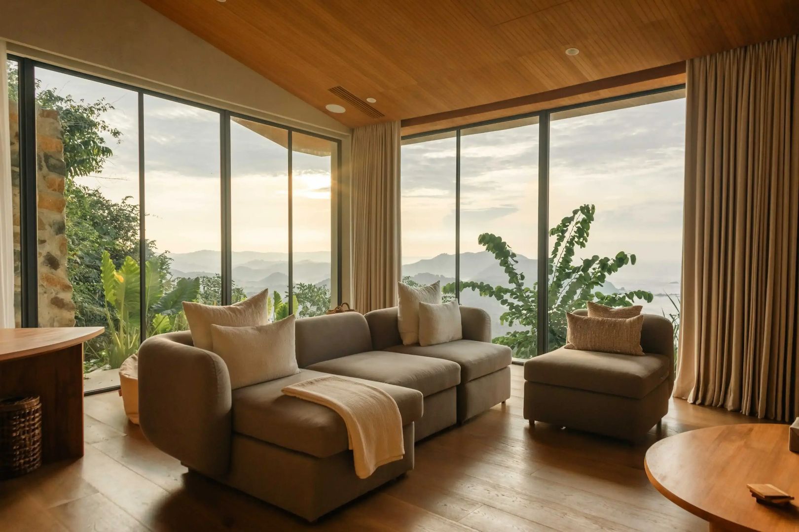 Polstersofa vor bodentiefen Fenstern mit Aussicht auf Hügelketten.