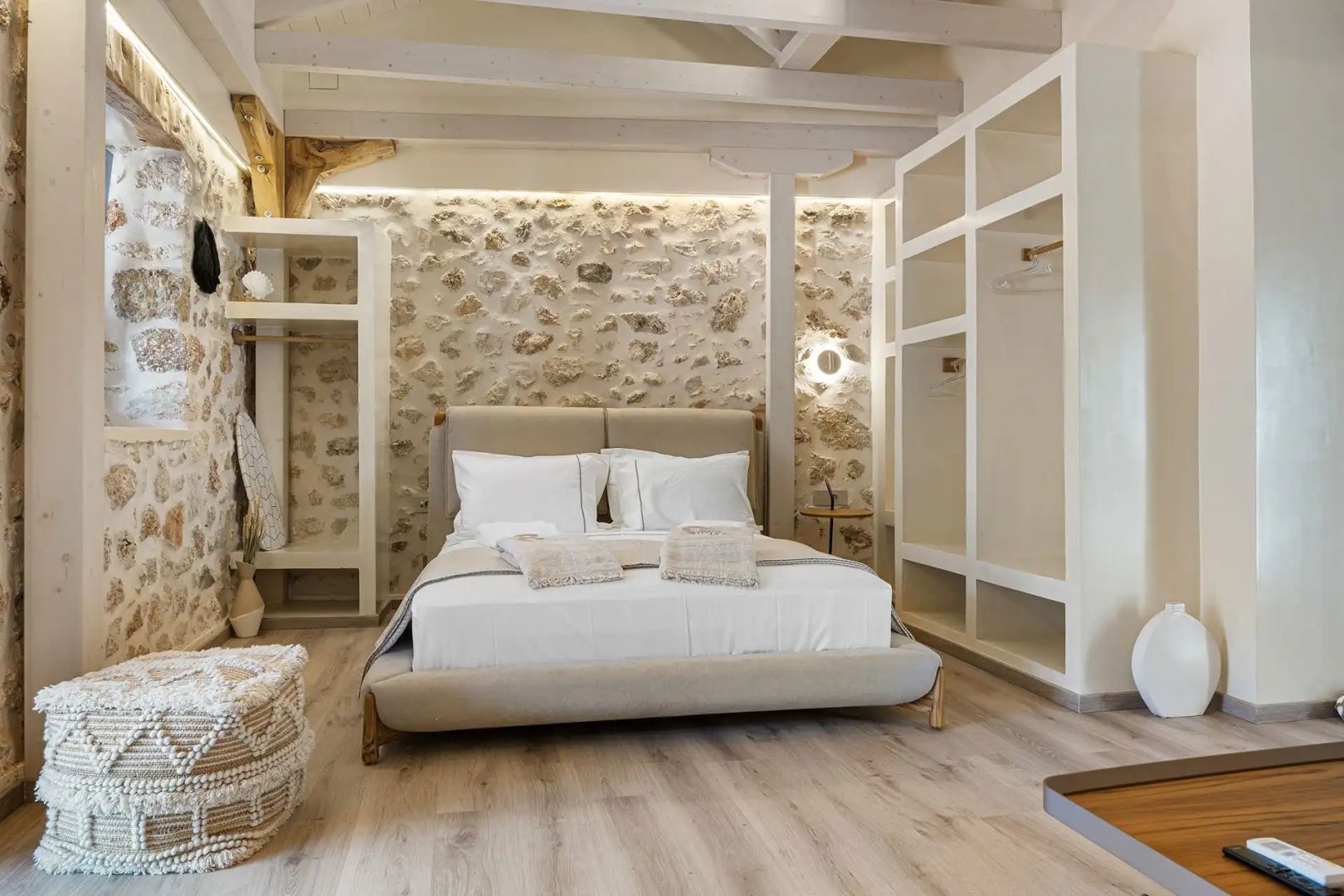 Schlafbereich mit Doppelbett, Natursteinwand und hellen Holzmöbeln unter dem Dach.