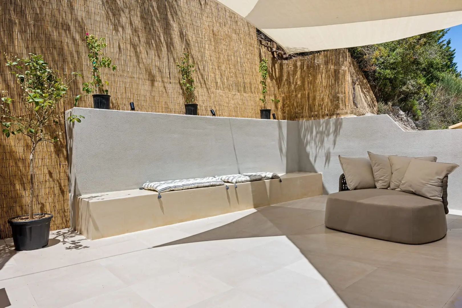 Terrasse mit einer gemauerten Sitzbank, Kissen und Schilfrohr als Sichtschutz.