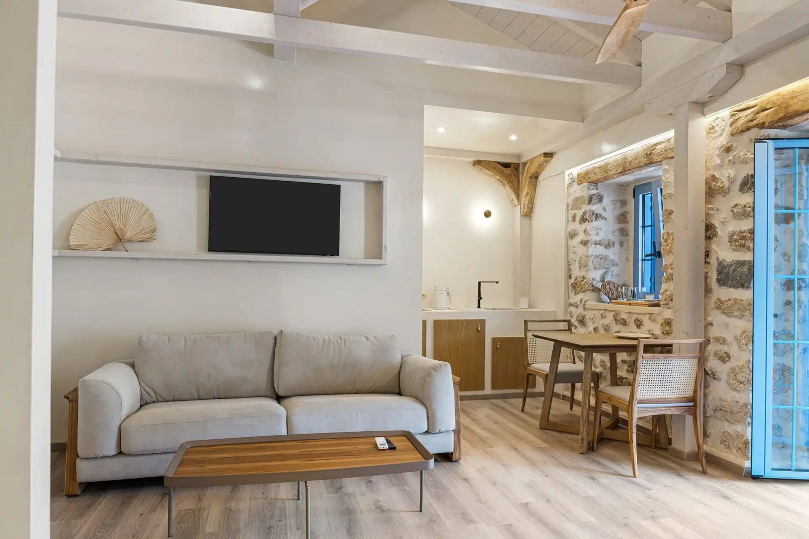 Wohnbereich mit beigem Sofa, Flachbildfernseher an der Wand und angrenzender Essecke.