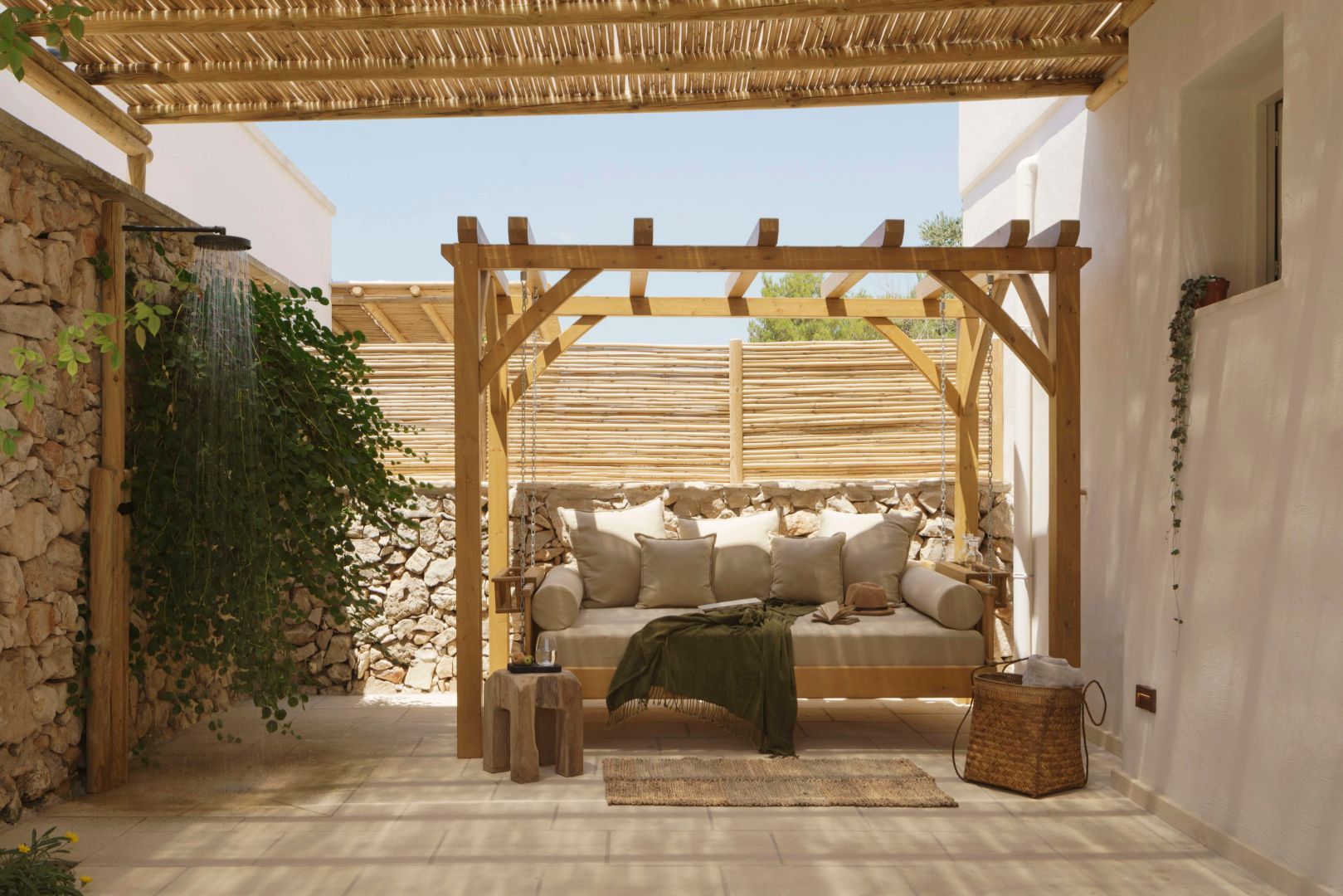 Überdachte Terrasse mit hängender Holzliege, Kissen und Bambuszaun im Außenbereich.