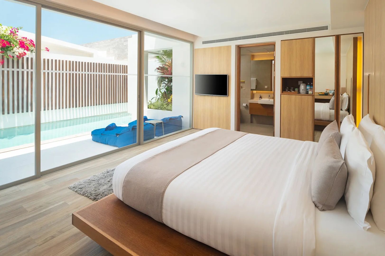 Schlafzimmer mit Doppelbett, Fernseher und Blick auf die Terrasse mit blauen Sitzkissen.