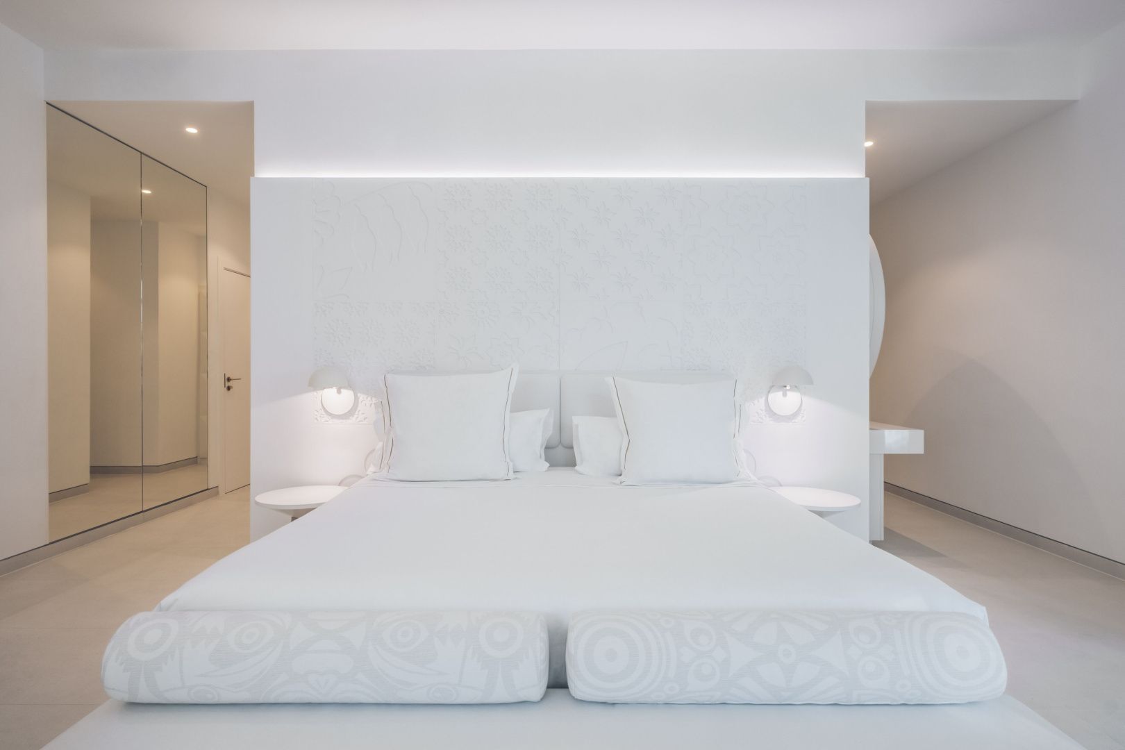 Modernes weißes Doppelbett mit beleuchteter Kopfteilwand und zwei Kissen.