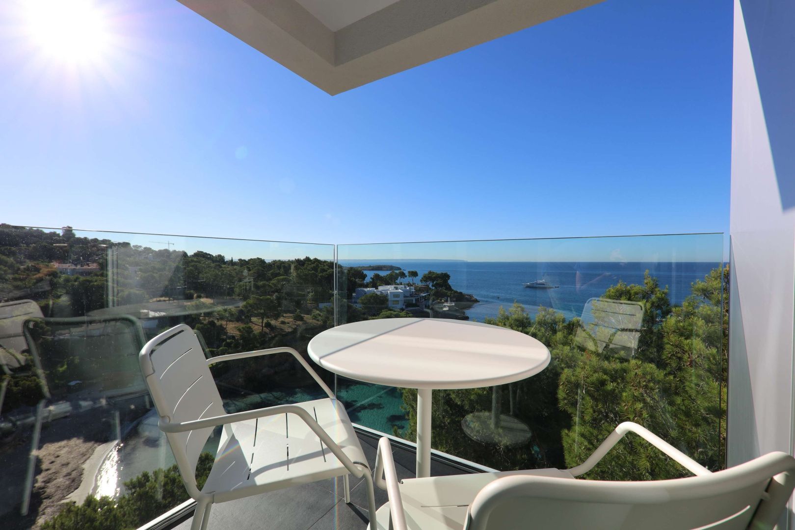 Sitzgruppe auf einem Hotelbalkon mit Glasbrüstung und Blick auf das Meer und die Küste.