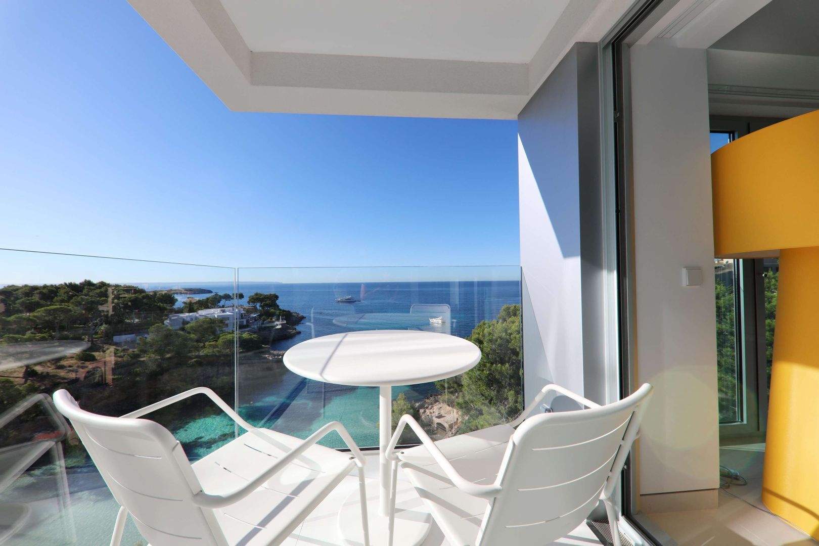 Zwei weiße Stühle und ein runder Tisch auf dem Balkon mit Blick auf das blaue Meer.