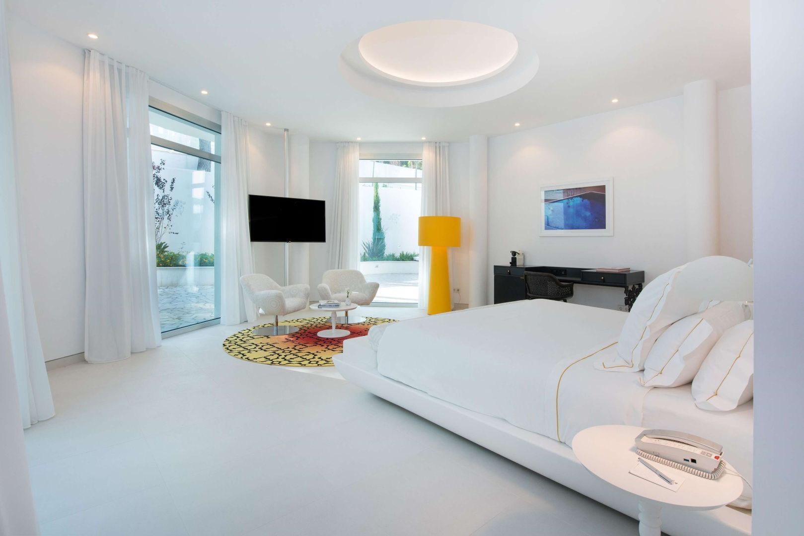 Weißes Zimmer mit großem Doppelbett, gelber Stehlampe und runder Vertiefung an der Decke.
