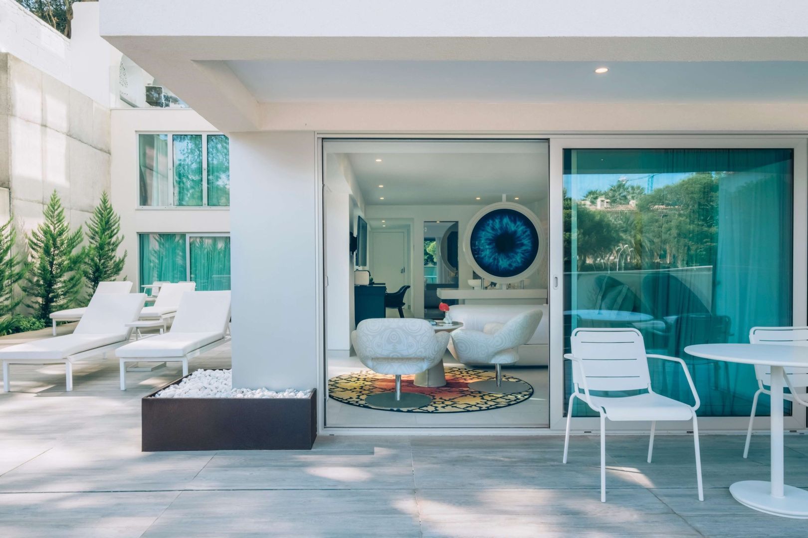 Blick von der Terrasse in ein Zimmer mit weißen Sesseln und einem runden Teppich.