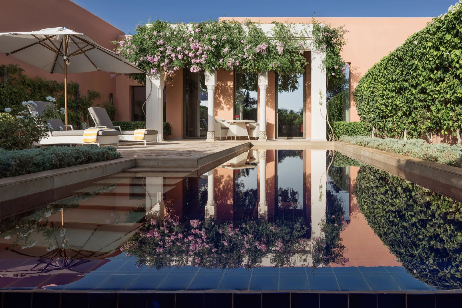 Privater Pool vor einem terrakottafarbenen Gebäude mit bewachsenen Säulen und Wasserspiegelung.
