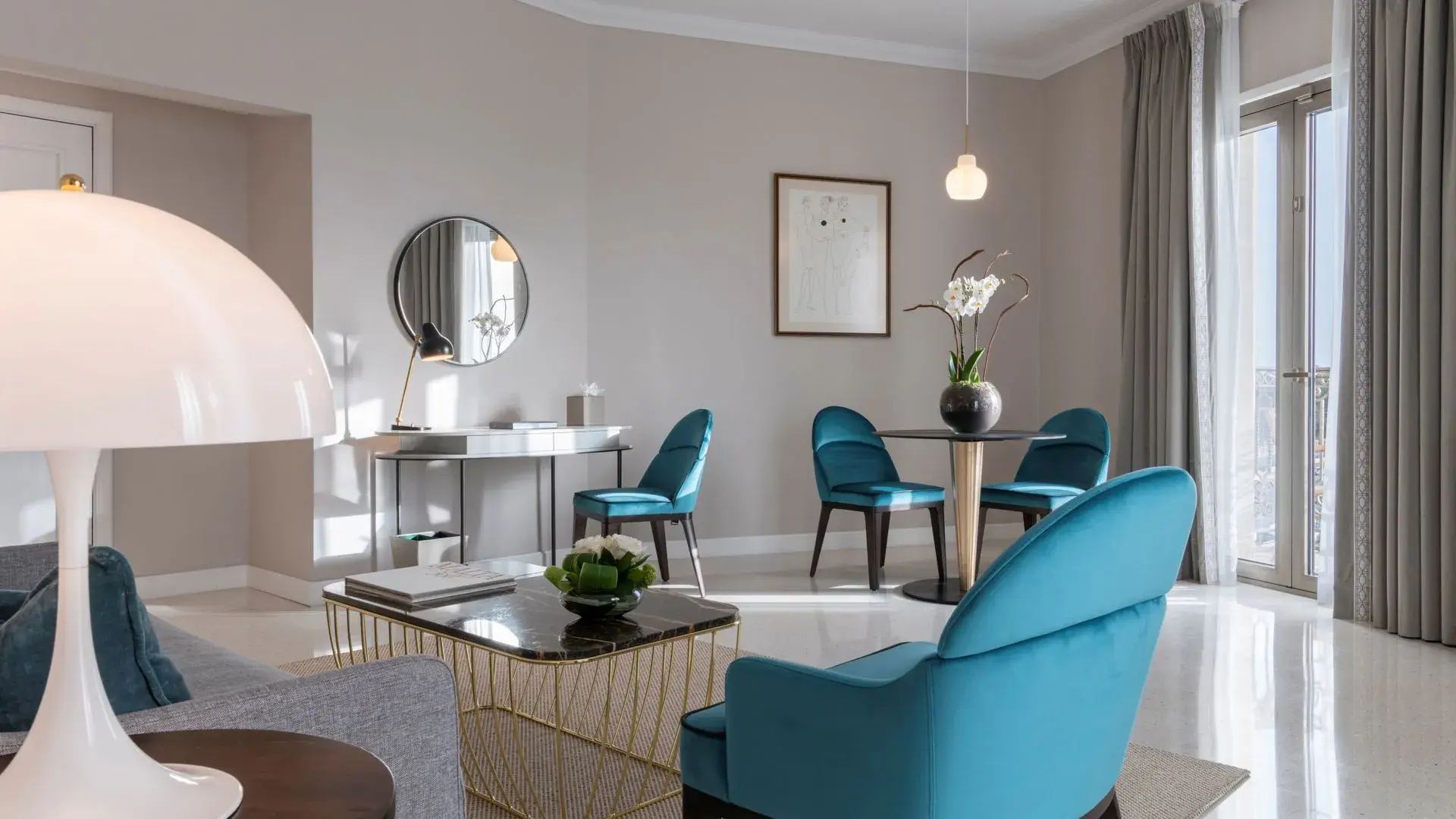 Wohnbereich im Hotelzimmer mit blauen Samtsesseln, einem kleinen Esstisch und Schminktisch.