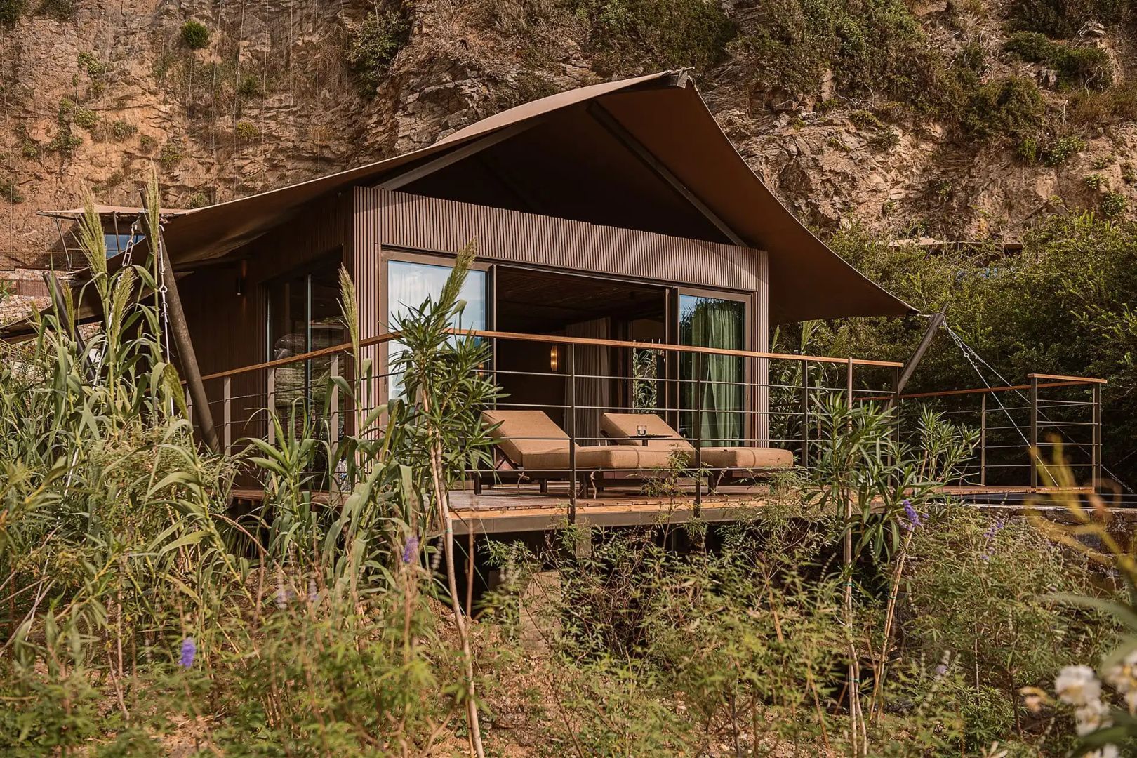 Zeltartige Villa aus Holz an einem Felsenhang mit eigener Holzterrasse und Liegen.